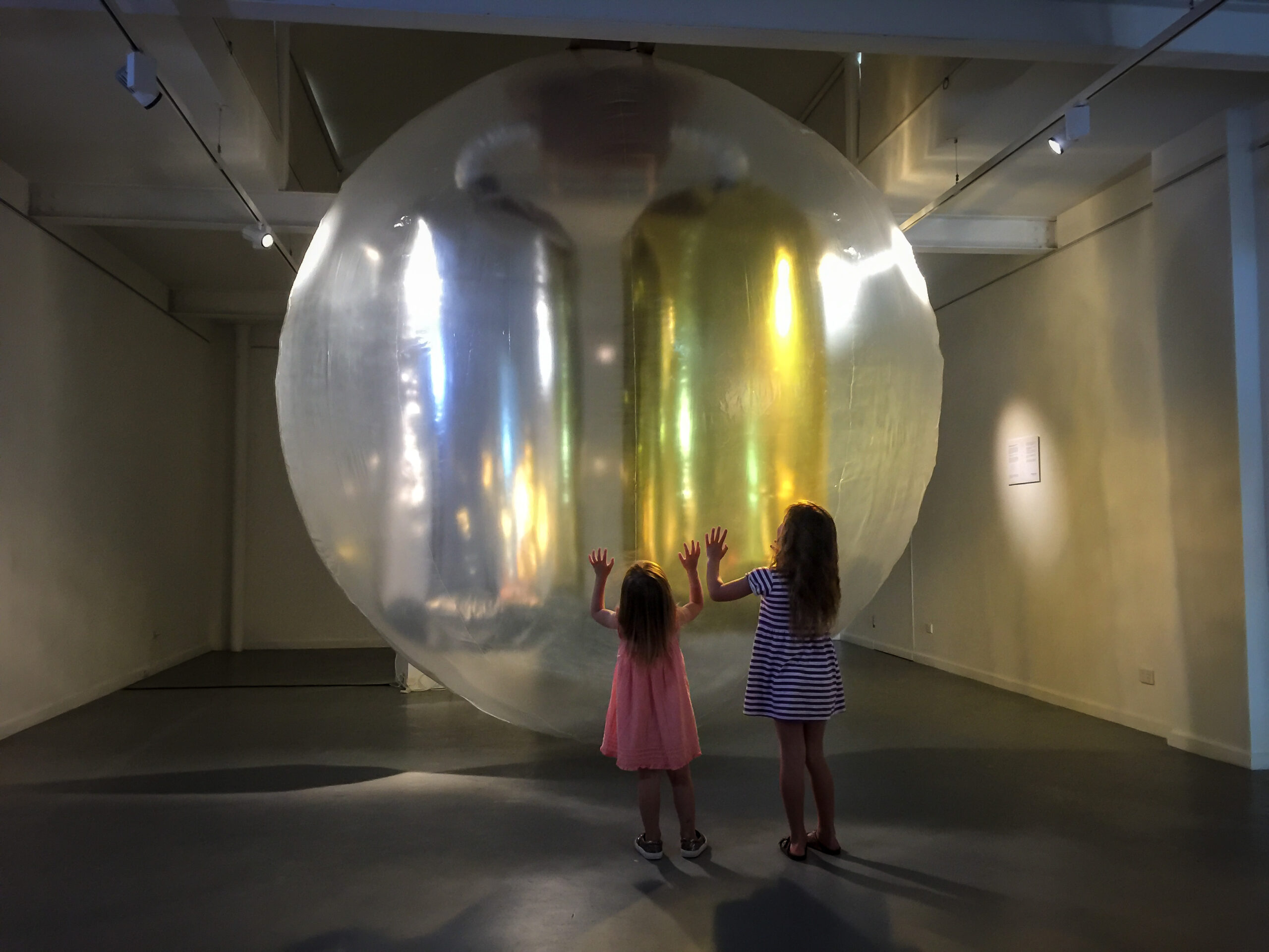 two young girls touching an artwork which looks like a big see threw ball in the gallery